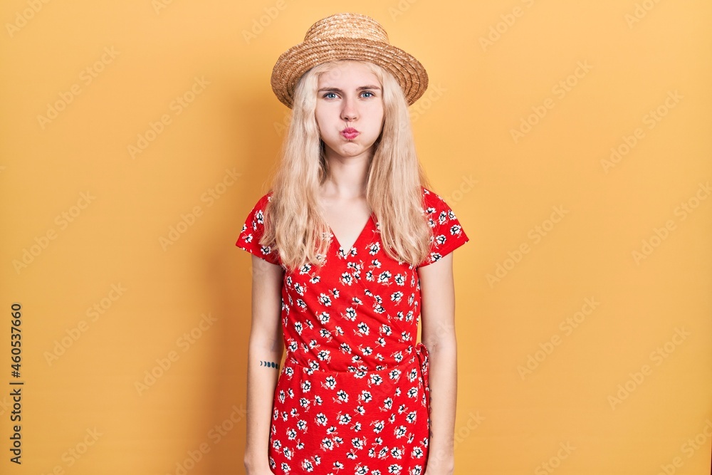 Beautiful caucasian woman with blond hair wearing summer hat puffing cheeks with funny face. mouth inflated with air, crazy expression. Beautiful caucasian woman with blond hair wearing summer hat puffing cheeks with funny face. mouth inflated with air, crazy expression.
