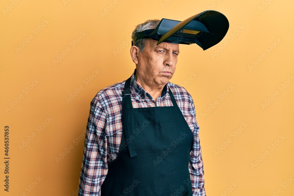 Handsome senior man with grey hair wearing welding protection mask skeptic and nervous, frowning upset because of problem. negative person.