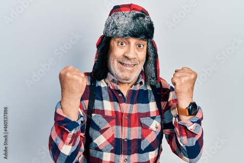 Fotografie Handsome mature man wearing winter hat with ear flaps screaming proud, celebrati