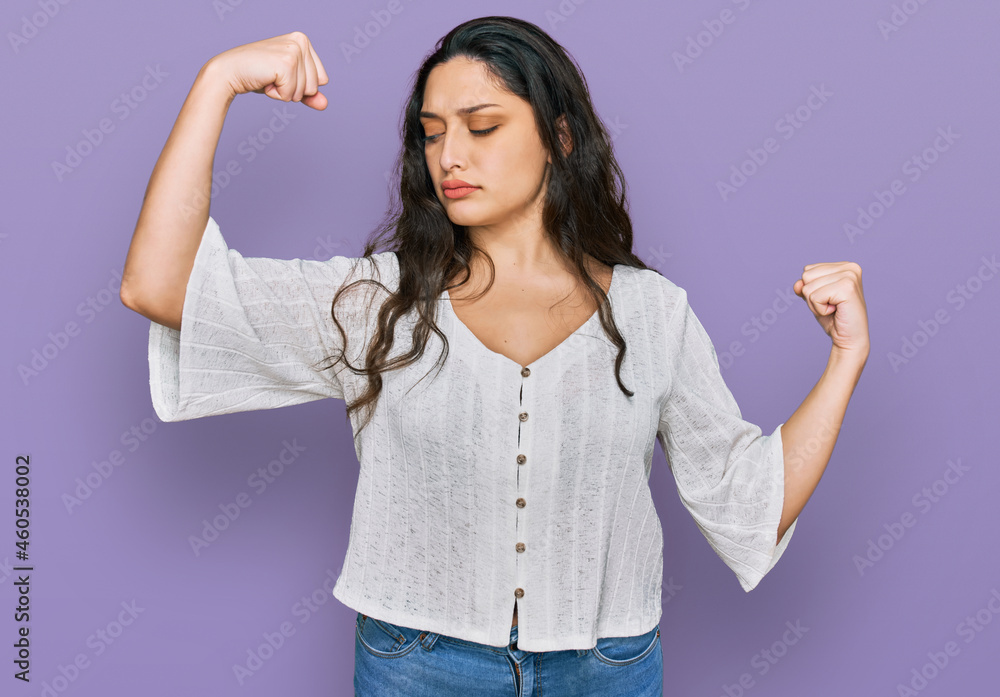 Obraz premium Brunette young woman wearing casual clothes showing arms muscles smiling proud. fitness concept.