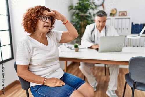 Senior woman sitting at doctor appointment very happy and smiling looking far away with hand over head. searching concept.