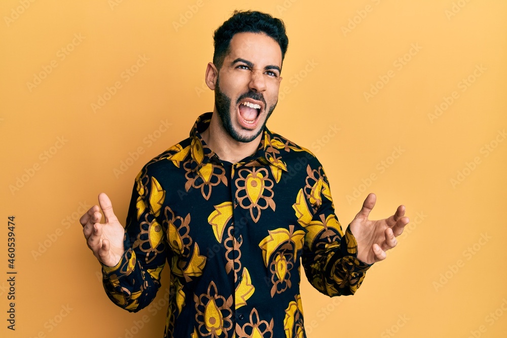 Young hispanic man wearing casual shirt crazy and mad shouting and yelling with aggressive expression and arms raised. frustration concept.