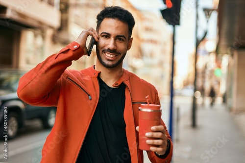 Young hispanic man talking on the smartphone drinking coffee at the city.