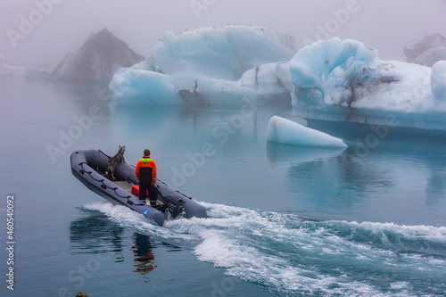 фотографія A rescue staff with a rescue dog riding a rubber patrol boat in the frigid waters and ice beg laden  of Glacier lagoon , Jokulsarlon ,Iceland