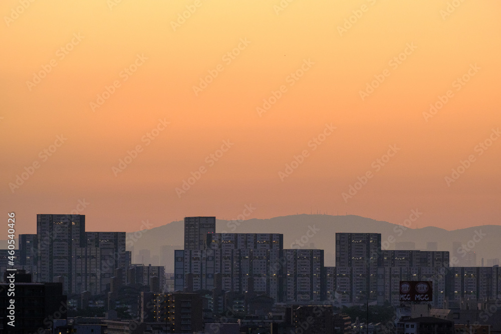 都市の夜明け、早朝ビルの隙間から太陽が昇り辺りはオレンジ色に染まる。ビルはシルエットに浮かぶ