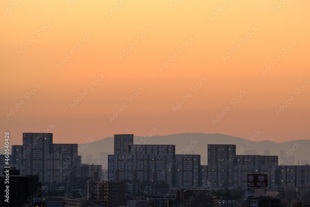 都市の夜明け、早朝ビルの隙間から太陽が昇り辺りはオレンジ色に染まる。ビルはシルエットに浮かぶ 都市の夜明け、早朝ビルの隙間から太陽が昇り辺りはオレンジ色に染まる。ビルはシルエットに浮かぶ