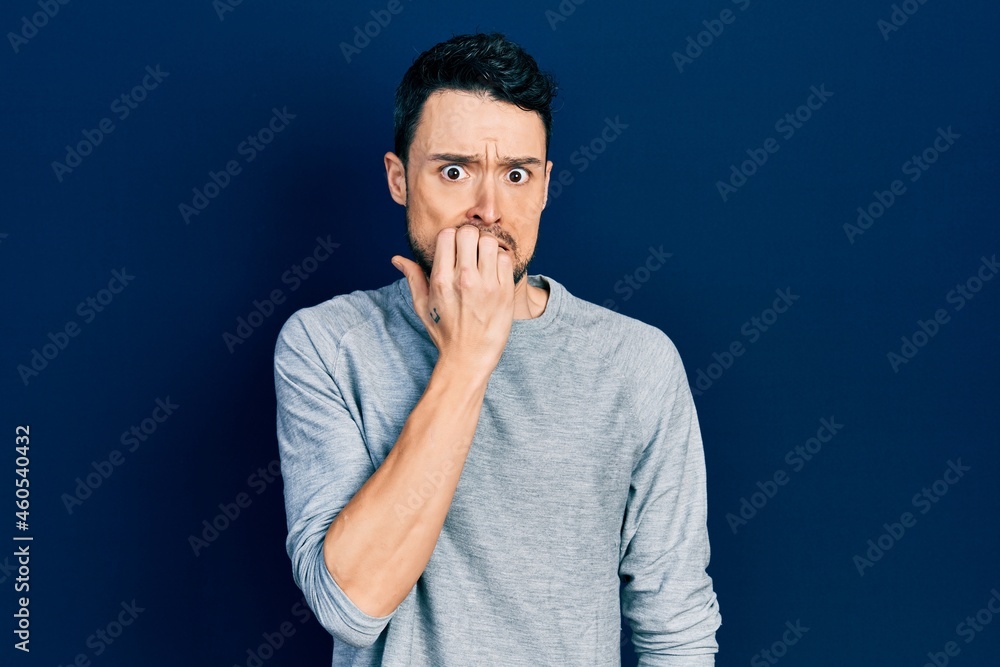 Young hispanic man wearing casual clothes looking stressed and nervous with hands on mouth biting nails. anxiety problem. Young hispanic man wearing casual clothes looking stressed and nervous with hands on mouth biting nails. anxiety problem.