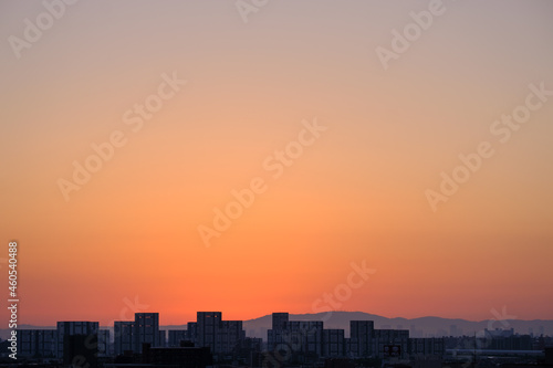 都市の夜明け、早朝ビルの隙間から太陽が昇り辺りはオレンジ色に染まる。ビルはシルエットに浮かぶ