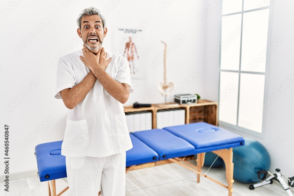 Middle age hispanic therapist man working at pain recovery clinic shouting suffocate because painful strangle. health problem. asphyxiate and suicide concept. Middle age hispanic therapist man working at pain recovery clinic shouting suffocate because painful strangle. health problem. asphyxiate and suicide concept.
