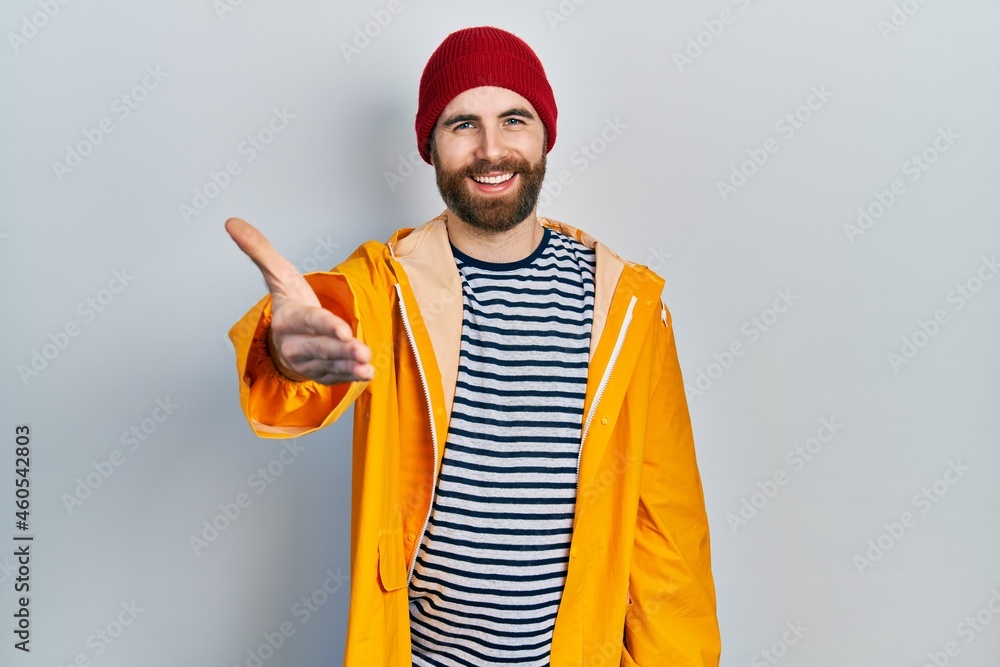 Caucasian man with beard wearing yellow raincoat smiling friendly offering handshake as greeting and welcoming. successful business. Caucasian man with beard wearing yellow raincoat smiling friendly offering handshake as greeting and welcoming. successful business.