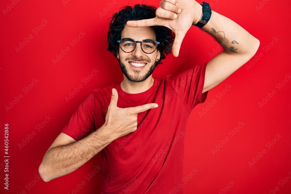 Handsome hispanic man wearing casual t shirt and glasses smiling making frame with hands and fingers with happy face. creativity and photography concept. Handsome hispanic man wearing casual t shirt and glasses smiling making frame with hands and fingers with happy face. creativity and photography concept.