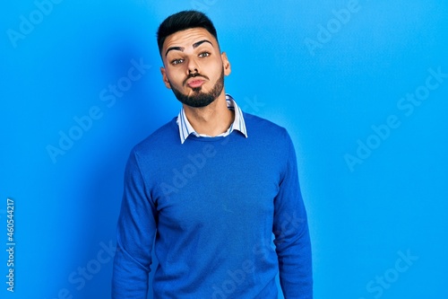 Young hispanic man with beard wearing casual blue sweater looking at the camera blowing a kiss on air being lovely and sexy. love expression.