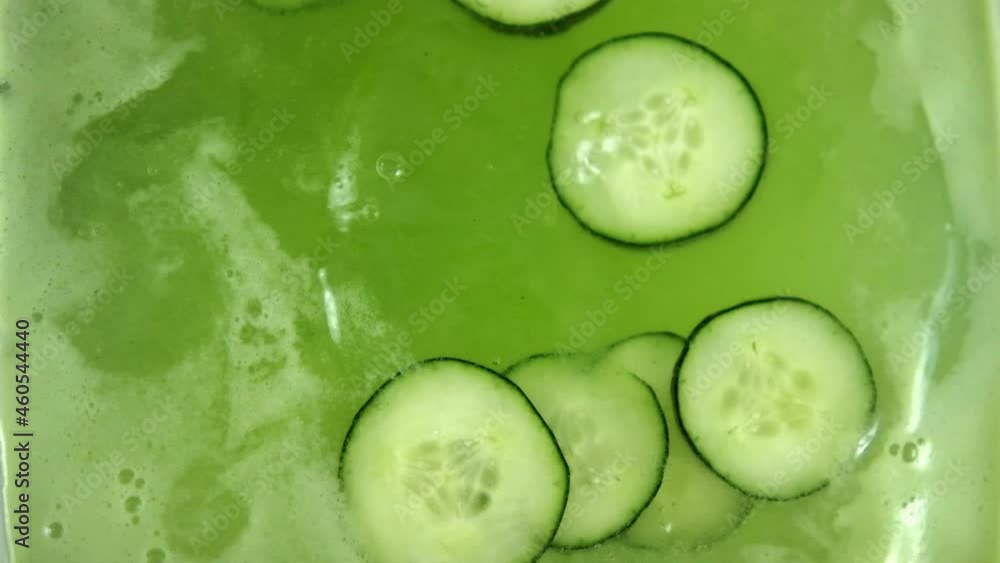 Dropping big piece of ice into refreshing cucumber drink in glass container Dropping big piece of ice into refreshing cucumber drink in glass container