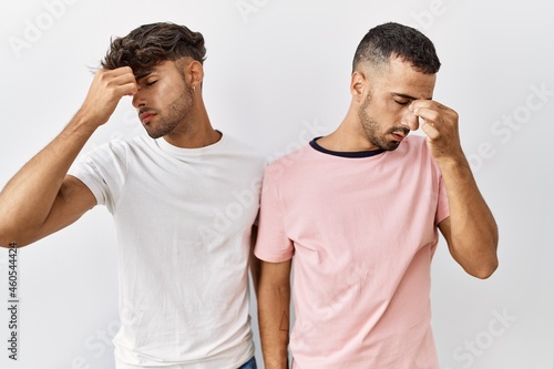 Young gay couple standing over isolated background tired rubbing nose and eyes feeling fatigue and headache. stress and frustration concept.