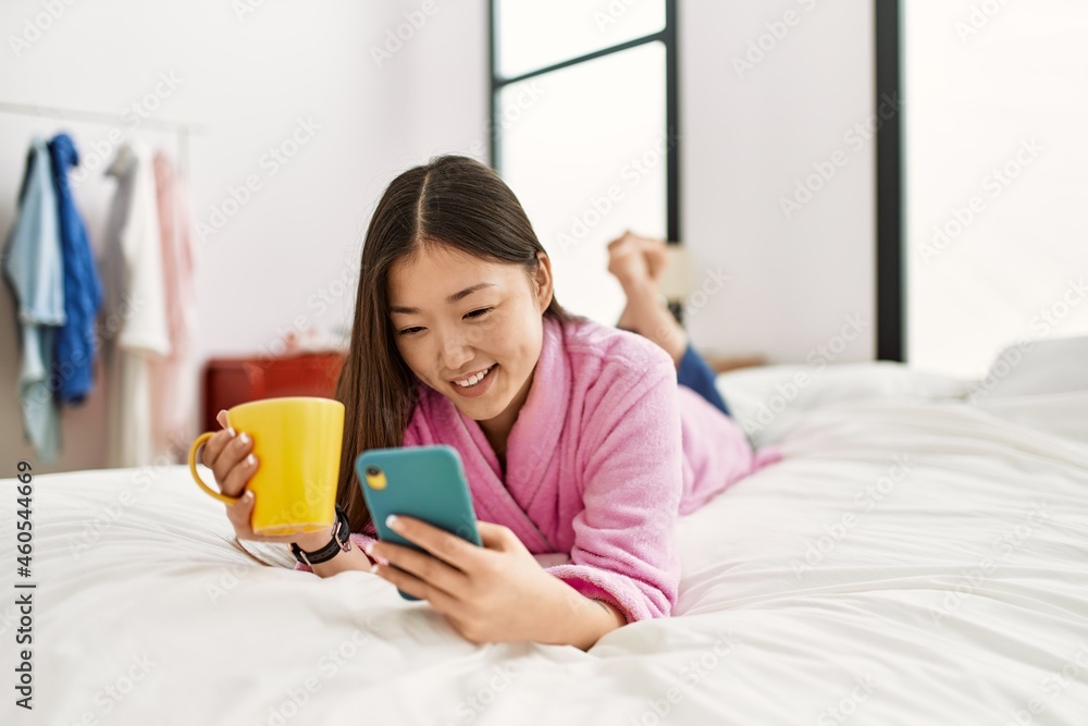Young chinese girl using smartphone and drinking coffee lying on the bed at bedroom. Young chinese girl using smartphone and drinking coffee lying on the bed at bedroom.
