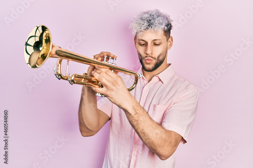Photography Young hispanic man with modern dyed hair playing trumpet making fish face with mouth and squinting eyes, crazy and comical