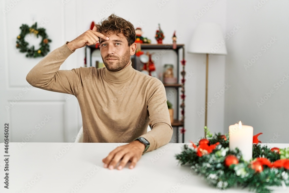 Young handsome man with beard sitting on the table by christmas decoration pointing unhappy to pimple on forehead, ugly infection of blackhead. acne and skin problem Young handsome man with beard sitting on the table by christmas decoration pointing unhappy to pimple on forehead, ugly infection of blackhead. acne and skin problem
