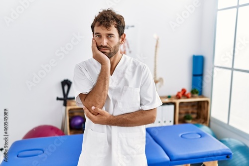Young handsome physiotherapist man working at pain recovery clinic thinking looking tired and bored with depression problems with crossed arms.