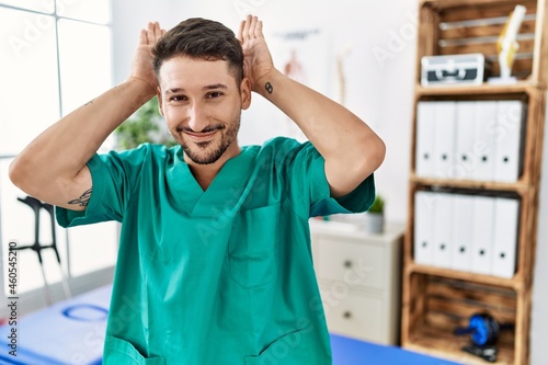 Young physiotherapist man working at pain recovery clinic doing bunny ears gesture with hands palms looking cynical and skeptical. easter rabbit concept.