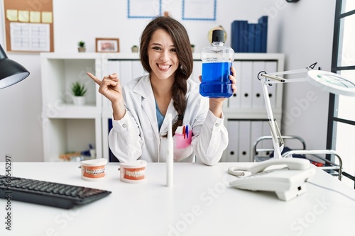 Young dentist woman holding mouthwash for fresh breath smiling happy pointing with hand and finger to the side