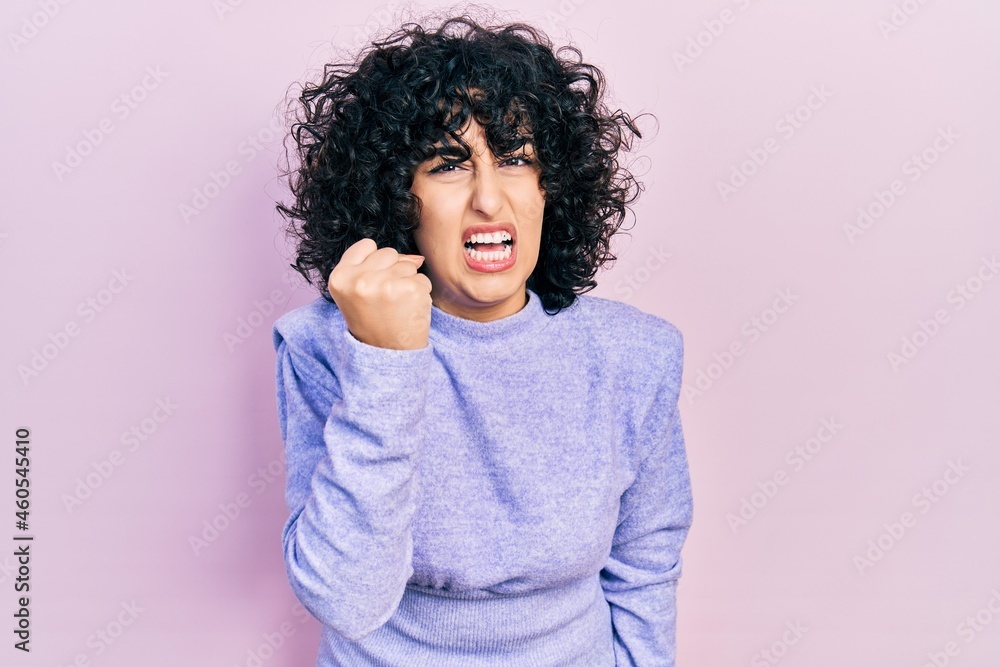 Young middle east woman wearing casual clothes angry and mad raising fist frustrated and furious while shouting with anger. rage and aggressive concept. Young middle east woman wearing casual clothes angry and mad raising fist frustrated and furious while shouting with anger. rage and aggressive concept.