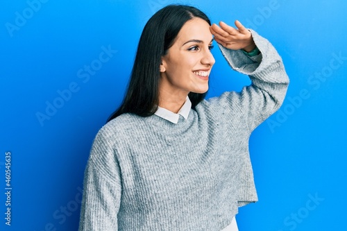 Young hispanic woman wearing casual clothes very happy and smiling looking far away with hand over head. searching concept.