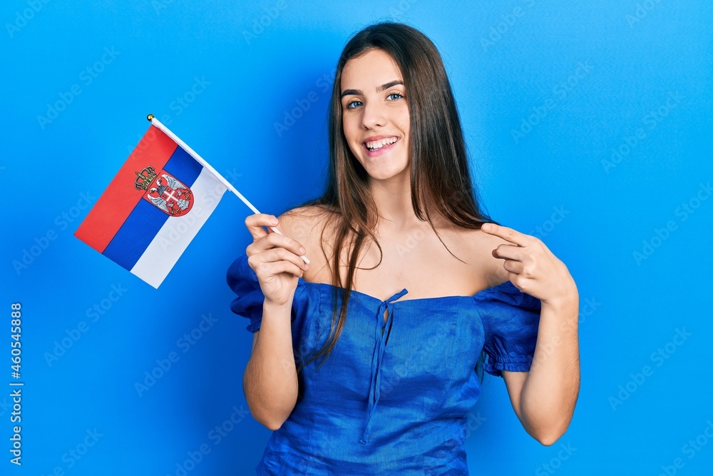 Young brunette teenager holding serbia flag smiling happy pointing with hand and finger Young brunette teenager holding serbia flag smiling happy pointing with hand and finger