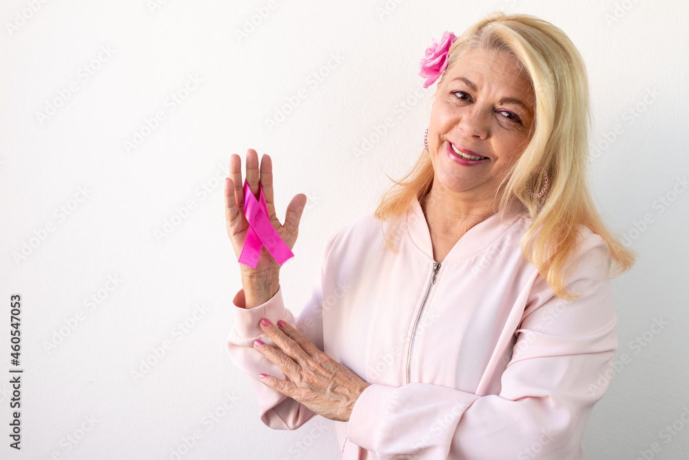 woman smiling looking forward holding pink october bow, campaign against breast cancer presence - obrazy, fototapety, plakaty 