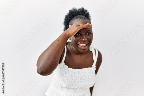 Young african woman standing over white isolated background very happy and smiling looking far away with hand over head. searching concept.