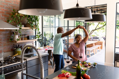 Happy african american senior couple dancing together in kitchen