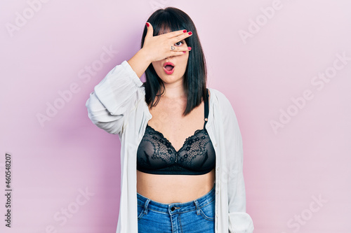 Young hispanic woman wearing lingerie peeking in shock covering face and eyes with hand, looking through fingers with embarrassed expression. © Krakenimages.com