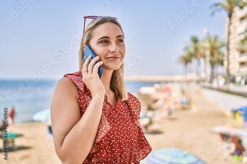 Young blonde girl smiling happy talking on the smartphone at the beach