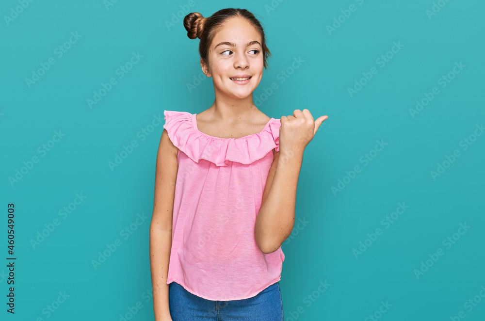 Beautiful brunette little girl wearing summer pink shirt smiling with happy face looking and pointing to the side with thumb up. Beautiful brunette little girl wearing summer pink shirt smiling with happy face looking and pointing to the side with thumb up.