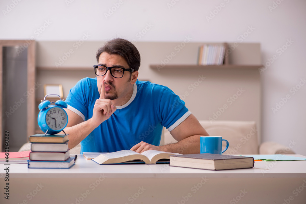 Young male student studying at home in time management concept Young male student studying at home in time management concept