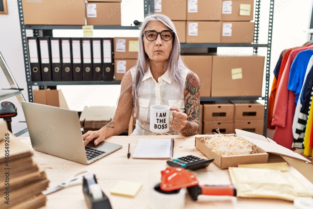 Middle age grey-haired woman working at the office drinking a cup of coffee thinking attitude and sober expression looking self confident Middle age grey-haired woman working at the office drinking a cup of coffee thinking attitude and sober expression looking self confident