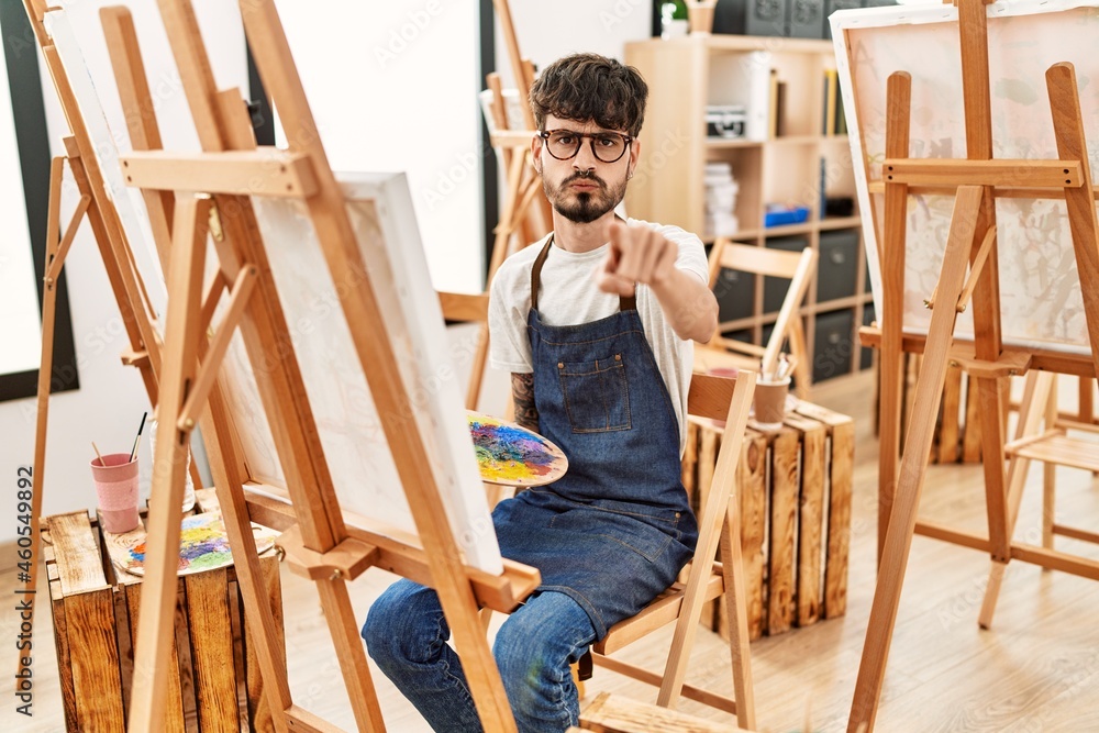 Hispanic man with beard at art studio pointing with finger to the camera and to you, confident gesture looking serious Hispanic man with beard at art studio pointing with finger to the camera and to you, confident gesture looking serious