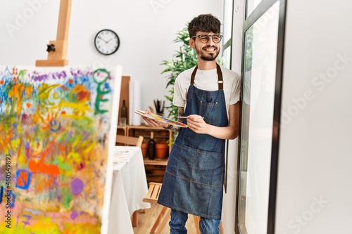 Young hispanic artist man smiling happy standing at art studio.