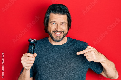 Middle age caucasian man holding electric razor machine pointing finger to one self smiling happy and proud