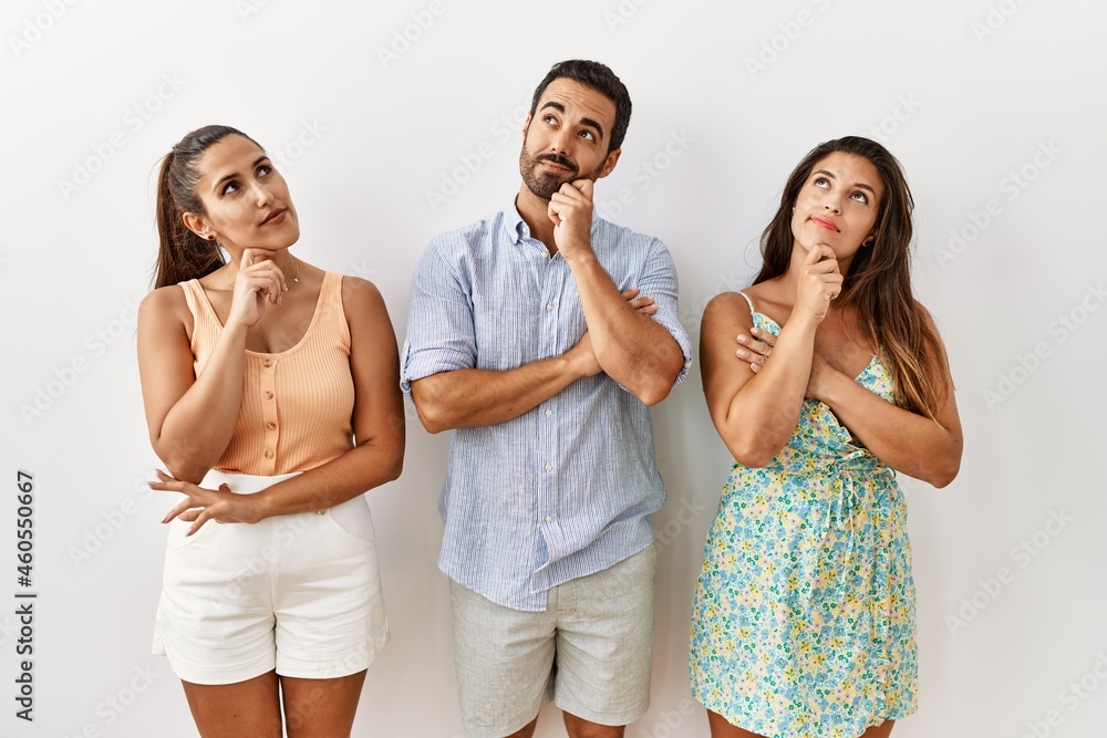 Group of young hispanic people standing over isolated background serious face thinking about question with hand on chin, thoughtful about confusing idea