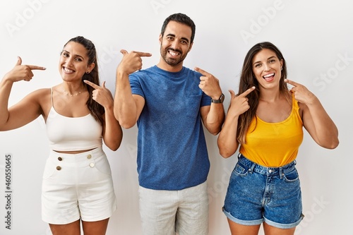 Group of young hispanic people standing over isolated background smiling cheerful showing and pointing with fingers teeth and mouth. dental health concept.