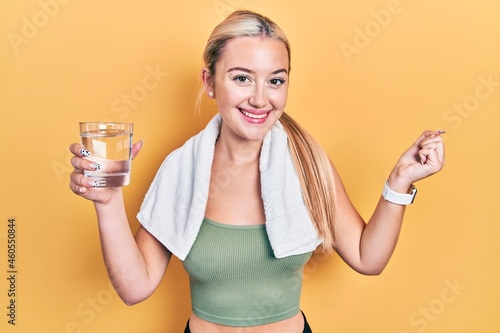 Young blonde girl wearing sportswear drinking glass of water screaming proud, celebrating victory and success very excited with raised arm © Krakenimages.com