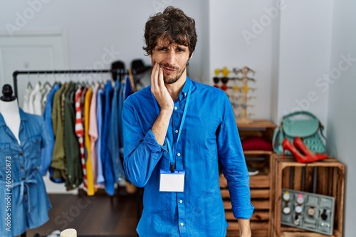 Young hispanic man working as manager at retail boutique touching mouth with hand with painful expression because of toothache or dental illness on teeth. dentist