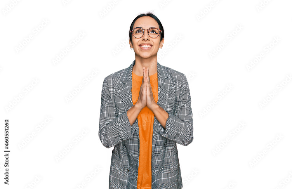 Young hispanic girl wearing business jacket and glasses begging and praying with hands together with hope expression on face very emotional and worried. begging. Young hispanic girl wearing business jacket and glasses begging and praying with hands together with hope expression on face very emotional and worried. begging.
