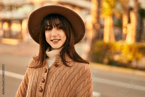 Brunette woman wearing winter hat smiling outdoors at the city on sunset © Krakenimages.com