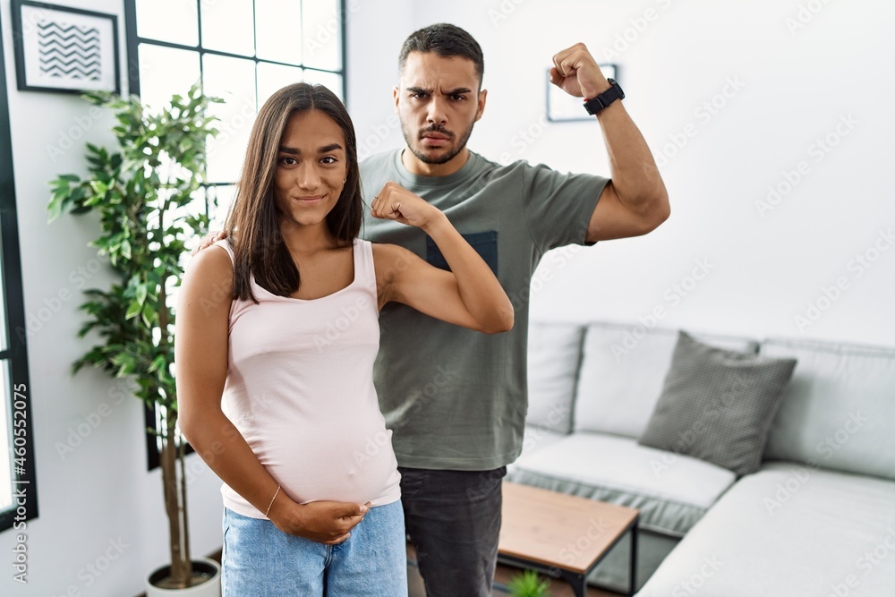 Young interracial couple expecting a baby, touching pregnant belly strong person showing arm muscle, confident and proud of power Young interracial couple expecting a baby, touching pregnant belly strong person showing arm muscle, confident and proud of power