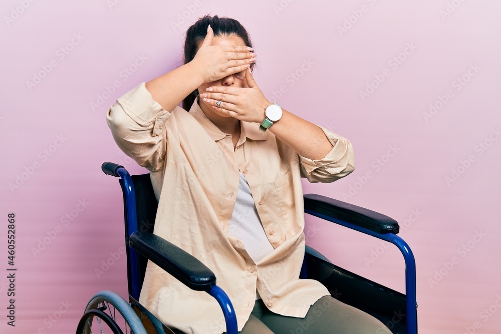 Young hispanic woman sitting on wheelchair covering eyes and mouth with hands, surprised and shocked. hiding emotion Young hispanic woman sitting on wheelchair covering eyes and mouth with hands, surprised and shocked. hiding emotion