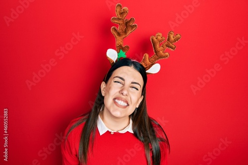 Young hispanic woman wearing cute christmas reindeer horns looking positive and happy standing and smiling with a confident smile showing teeth