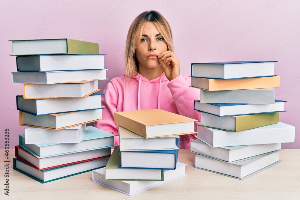 Young caucasian woman sitting on the table with books mouth and lips shut as zip with fingers. secret and silent, taboo talking Young caucasian woman sitting on the table with books mouth and lips shut as zip with fingers. secret and silent, taboo talking