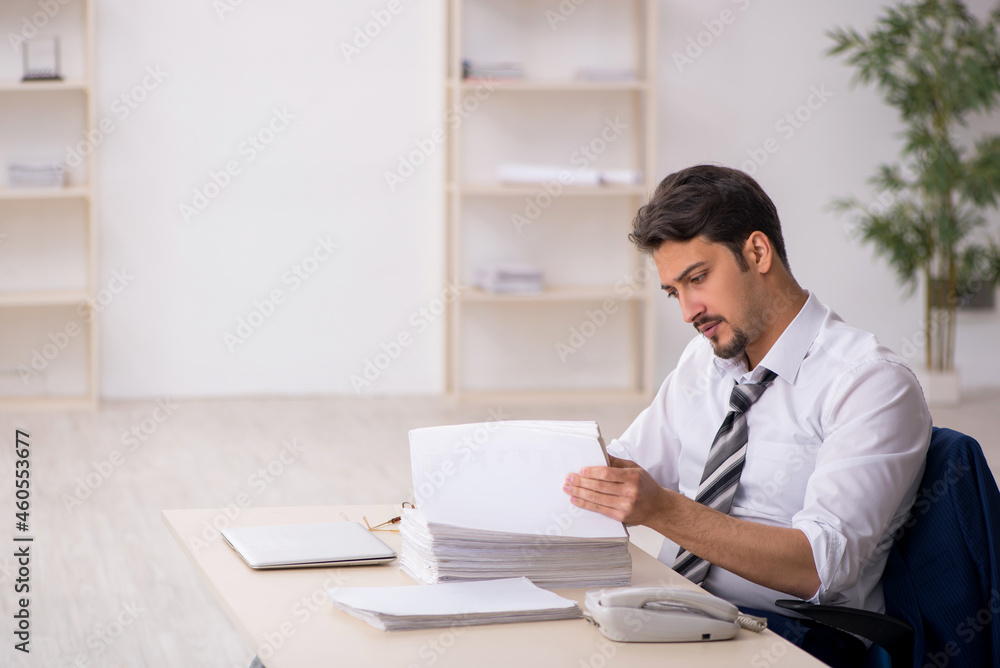 Young male employee unhappy with excessive work in the office Young male employee unhappy with excessive work in the office