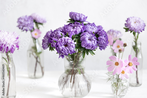 Glass vases with fresh chrysanthemum flowers on a blurred white background.
